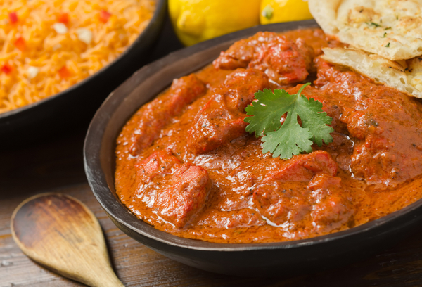A delicious bowl of creamy chicken tikka masala with rice, lemons, and naan bread.