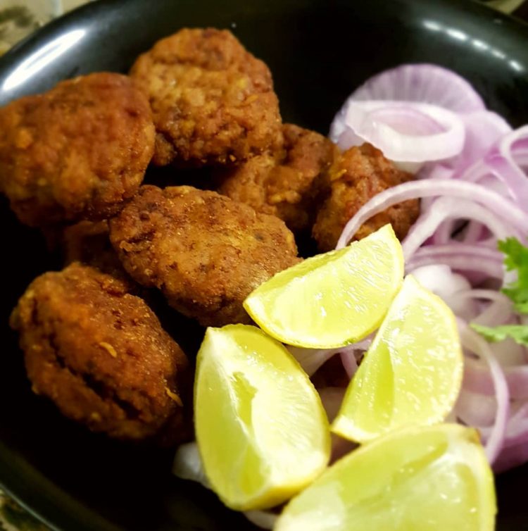Mutton Tikki next to wedges of lime and slices of onion