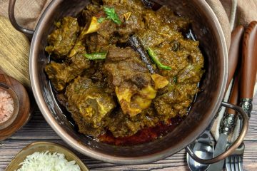 Green Mutton Curry in a kadhai with rice and whole spices on the side.