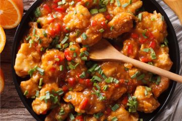 Mandarin Chicken in a black bowl with oranges on the side.