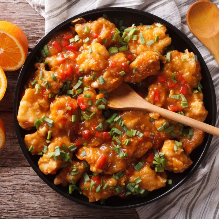 Mandarin Chicken in a black bowl with oranges on the side.