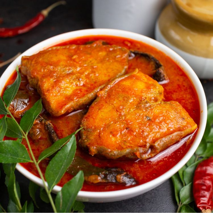 Basa Fish Curry in a white bowl with curry leaves and red chillies.