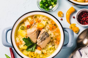 Fish soup in a blue ceramic bowl surrounded by vegetables
