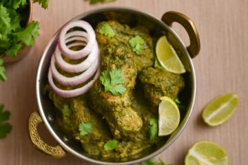 Hariyali Chicken Curry in a brass bowl with onions, lime wedges and coriander beside it