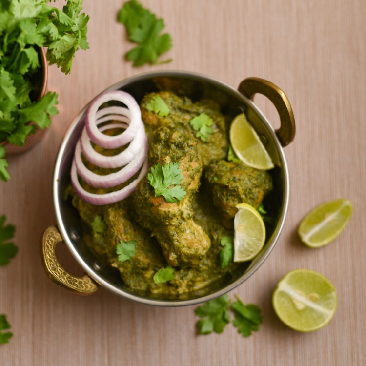 Hariyali Chicken Curry in a brass bowl with onions, lime wedges and coriander beside it