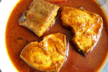 Rohu curry on a white plate next to curry leaves and dried red chilli