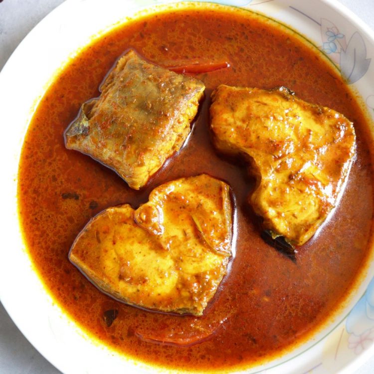 Rohu curry on a white plate next to curry leaves and dried red chilli