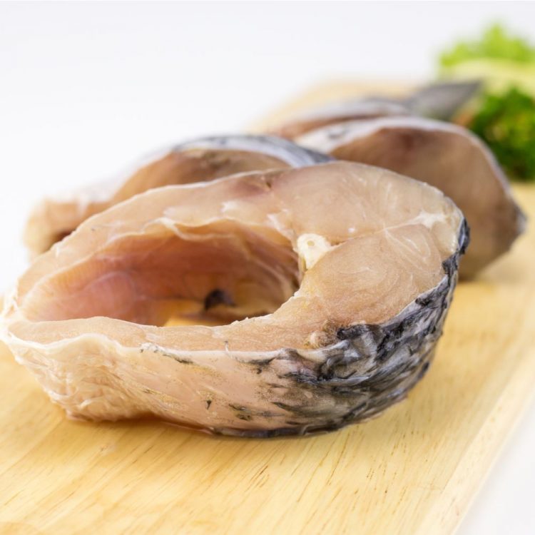 Rohu Fish cut into steaks on wooden board next to salad