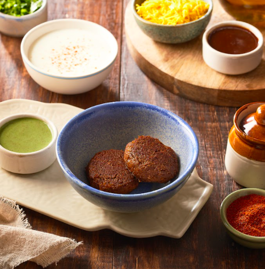 Two pieces of Glaouti kebabs in a blue bpwl with bowl of curd aand corriander chutney on the side.