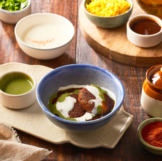 Galouti Kebab in a bowl topped with curd and tamarind chutney.